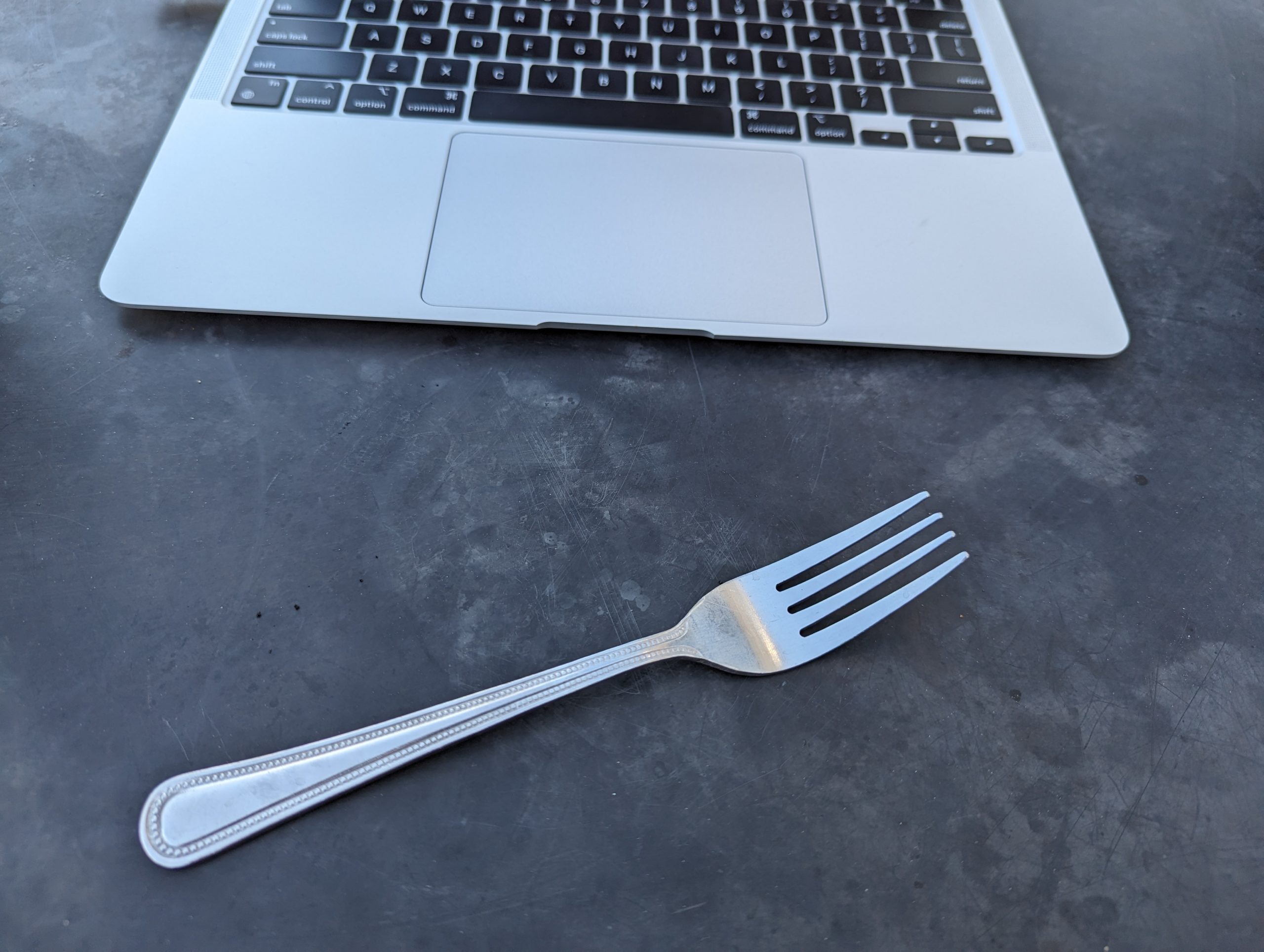 Metal fork in front of an underutilized Mac laptop
